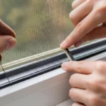 ช่างกำลังติดตั้งมุ้งลวดกันยุงที่กรอบหน้าต่างอย่างละเอียด